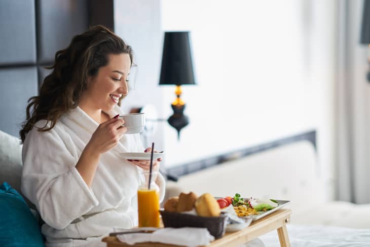 Woman sitting in bed at hotel eating breakfast in bed room service