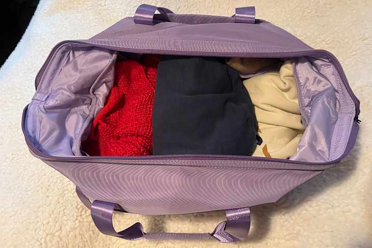 Lavender florence by mills x DELSEY PARIS Weekender Bag  duffel bag filled with a red sweater, dark clothing, and a beige item, resting on a soft surface.