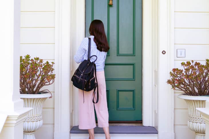 Back view of a woman carrying a backpack back to home using a key to open her front door