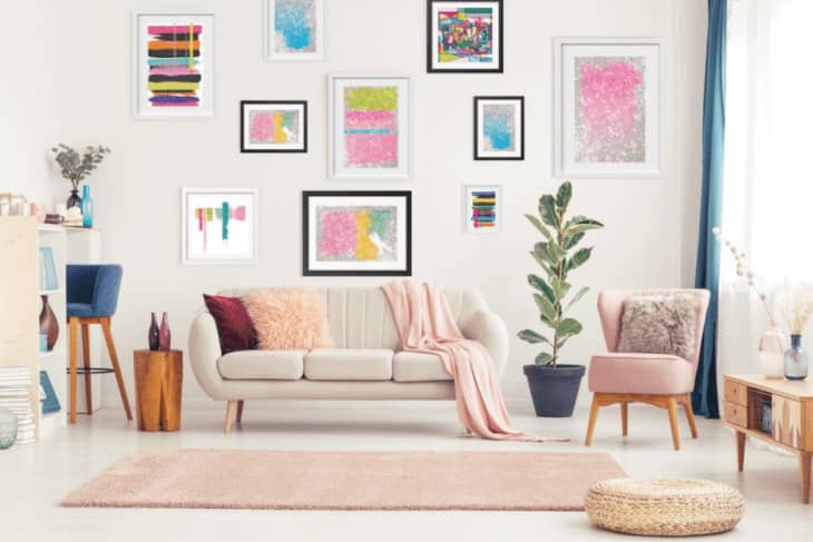Living room with a beige sofa, pink and blue cushions, abstract art on walls, and a potted plant.