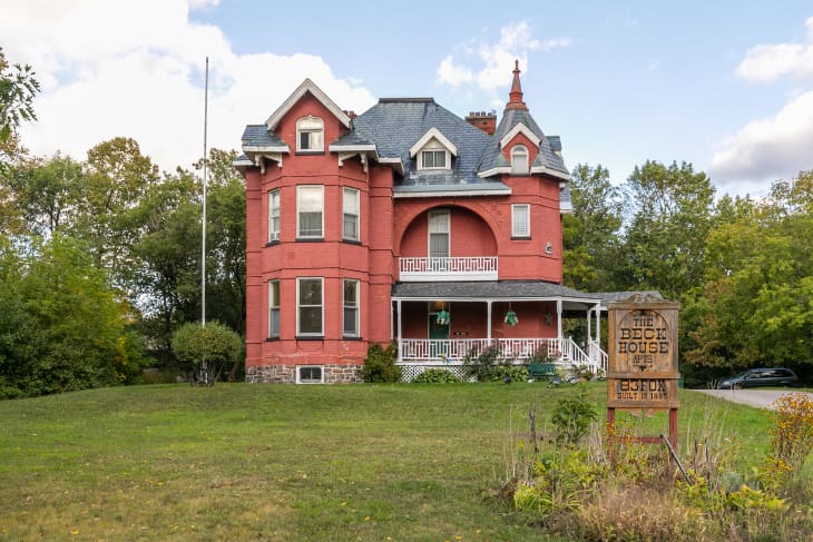 Victorian-style red brick house with a wraparound porch, surrounded by trees and a lawn, sign reads "The Beck House."