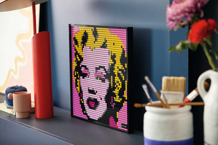 Pop art portrait made of small colored tiles on a shelf with art supplies and a pink flower.