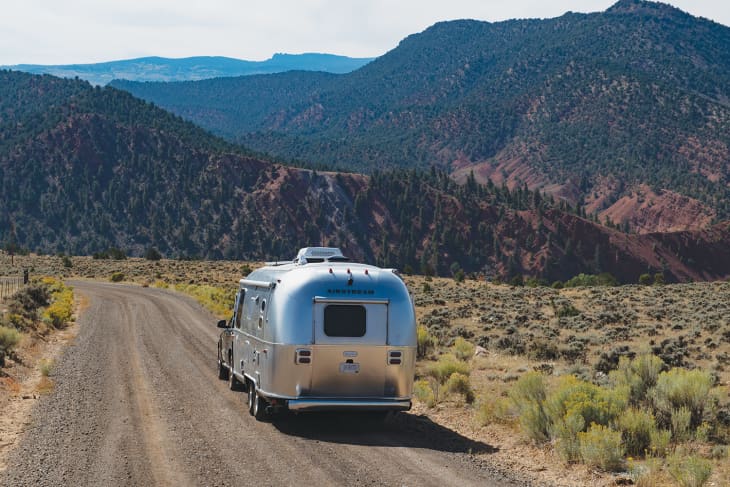 Airstream trailer on a dirt road surrounded by mountains and desert vegetation.