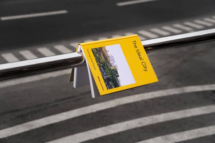 Yellow book titled "The Ideal City" hanging on a metal railing over a crosswalk.
