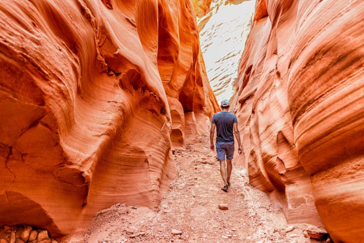 Person walking through a narrow red rock canyon with textured walls.