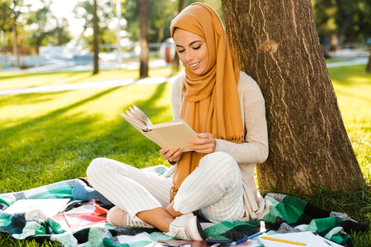 Woman wearing hijab sitting outside reading a book