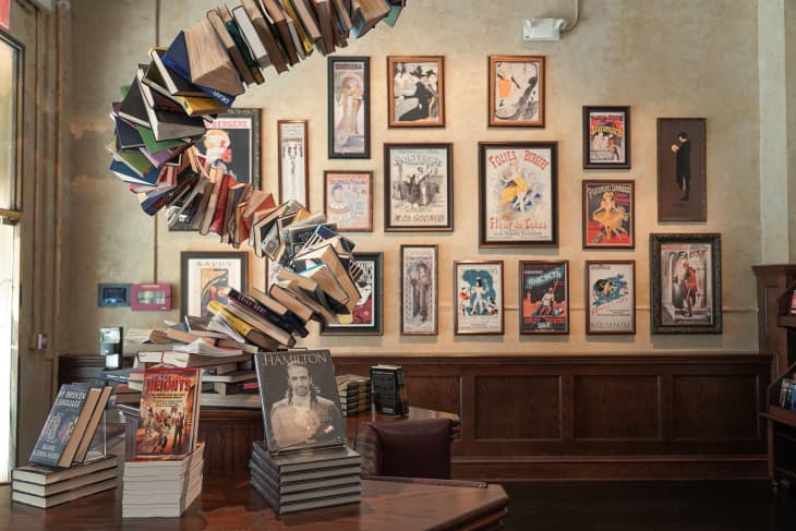 Books spiraling upward on a table with framed vintage posters on the wall in a cozy room.