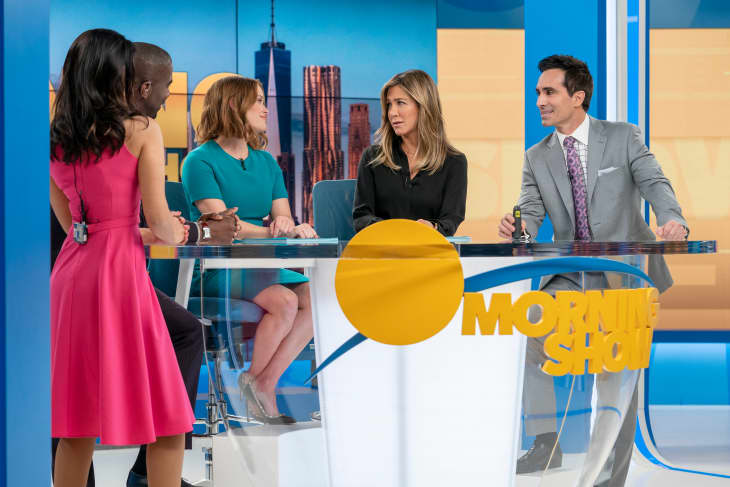 Four people discussing at a news desk with "Morning Show" logo, cityscape backdrop.