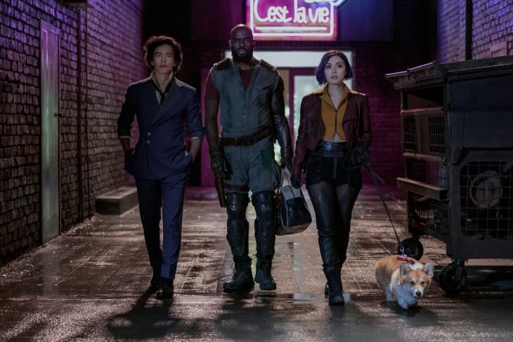 Three people walking in a dimly lit alley with a neon sign, accompanied by a small dog.