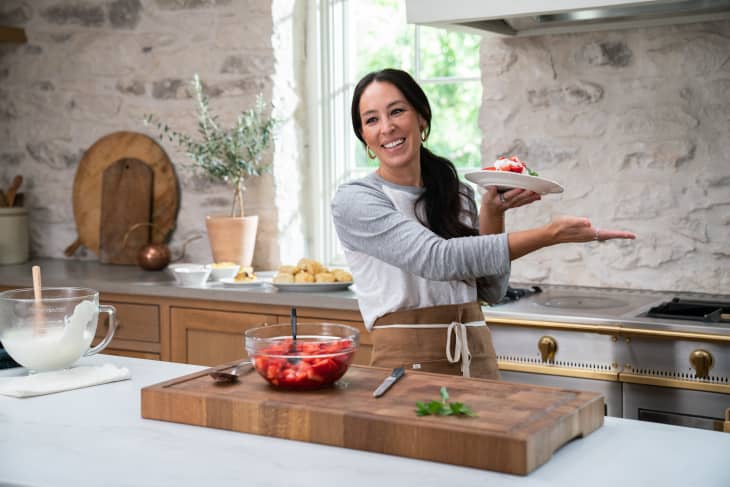 Woman in a kitchen holding a dessert plate, with strawberries and whipped cream on a cutting board.