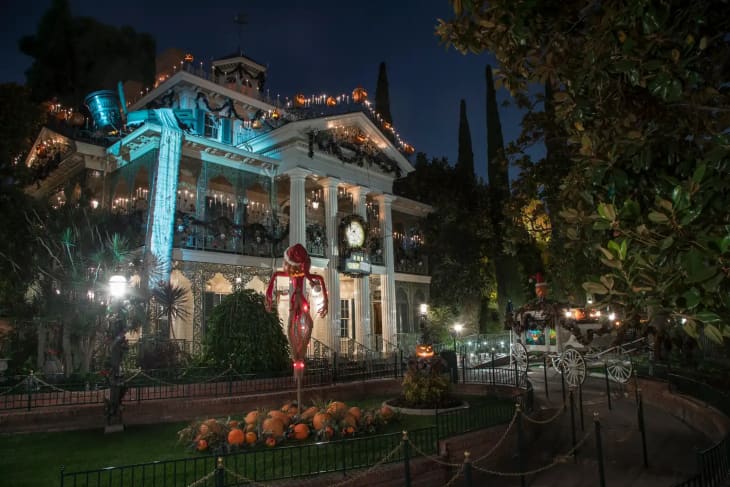 Haunted mansion at night with Halloween decorations, pumpkins, and a horse-drawn carriage.