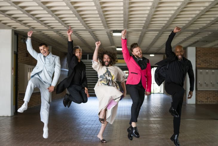 Five people jumping in a hallway, wearing colorful and stylish outfits, with arms raised in celebration.
