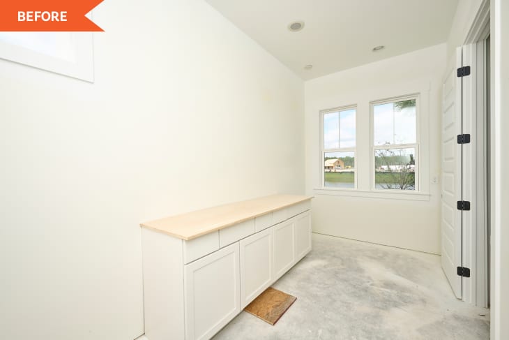 Unfinished laundry room with white cabinets, wooden countertop, and two windows overlooking a lake.