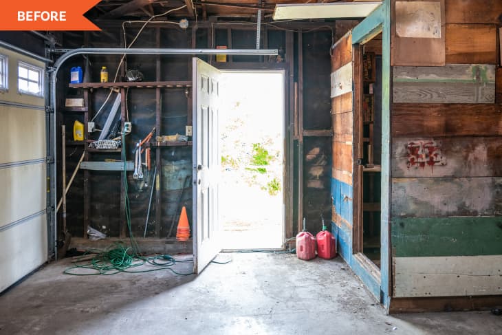 Cluttered garage with open door, exposed beams, shelves, tools, and two red gas cans on the floor.