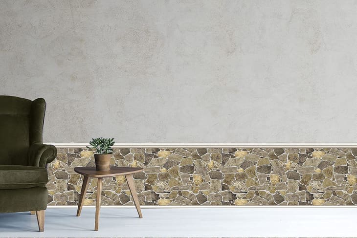 Olive green armchair and wooden side table with plant against a stone-patterned wall.