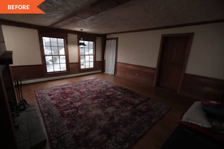 Dimly lit living room with large windows, red patterned rug, and wooden paneling.
