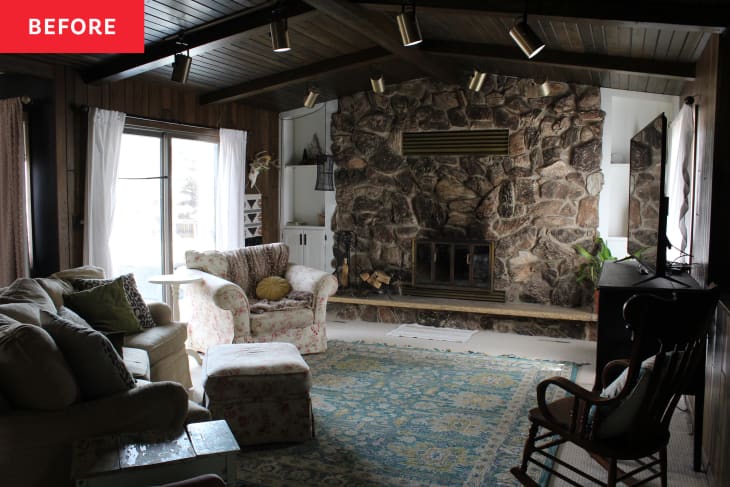 Cozy living room with stone fireplace, floral armchair, patterned rug, and sliding glass doors with white curtains.