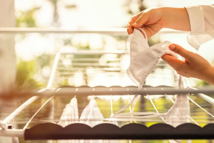 A person hanging a white garment on a drying rack outdoors, with sunlight filtering through greenery.