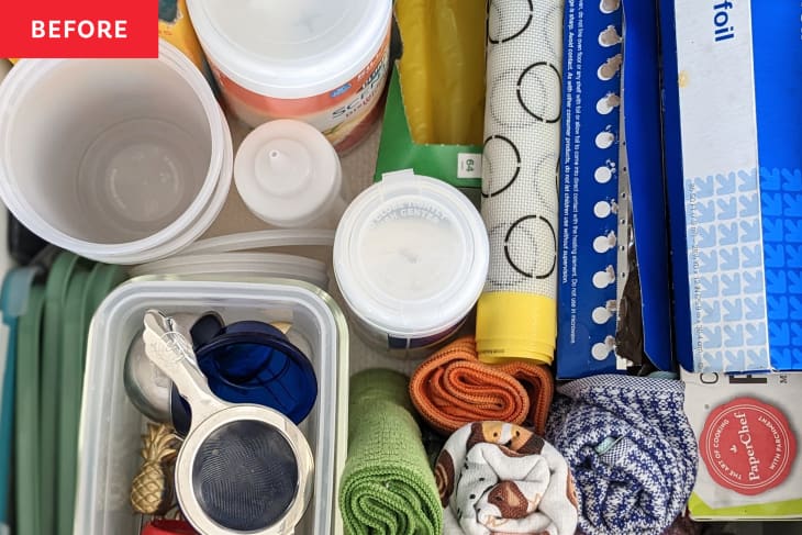 Kitchen drawer with plastic containers, foil, measuring spoons, and rolled dish towels.