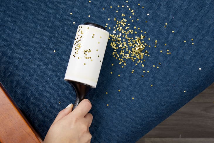 Angled view of a hand holding a lint roller and using it to clean up glitter on a chair cushion.