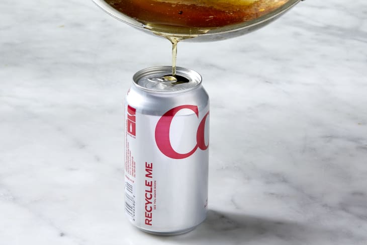 Angled shot of bacon grease being poured into a diet coke can on a white surface.