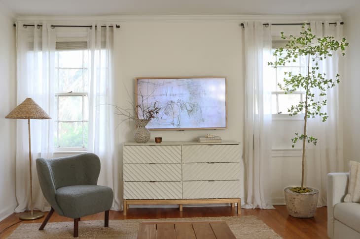 Living room with white walls, tall windows with white curtains, white dresser under TV instead of media console