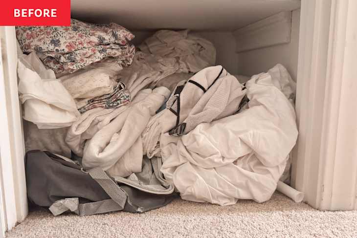 Cluttered storage space filled with wrinkled bedding, floral sheets, and a gray bag.