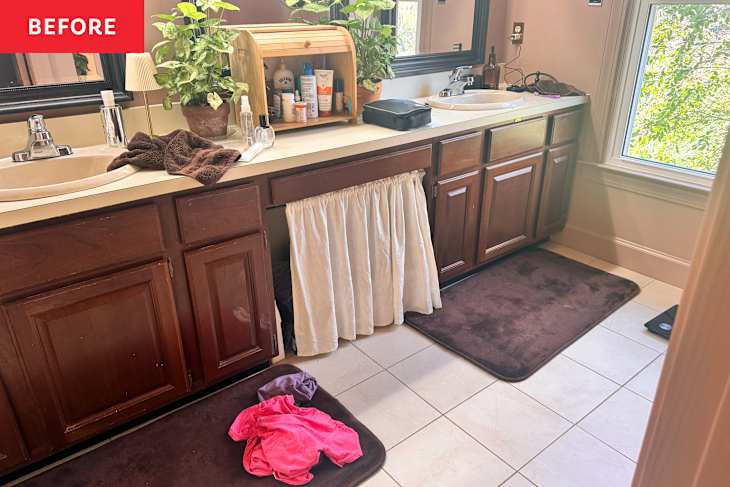 Bathroom vanity with double sinks, wooden cabinets, a potted plant, and towels on the counter; clothes on the floor.