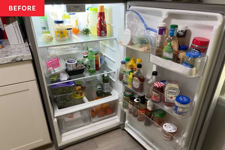 A cluttered refrigerator filled with various condiments, drinks, and fresh produce, including leafy greens and tomatoes.