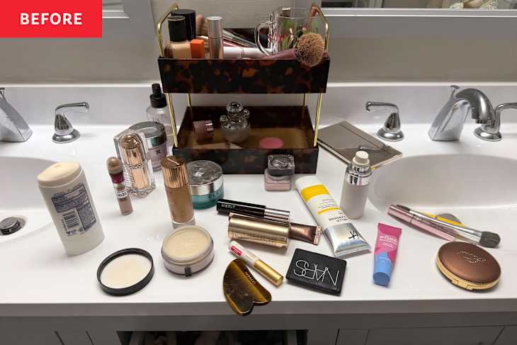 Cluttered bathroom countertop with various skincare and makeup products, including bottles, jars, and brushes.