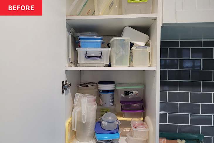 Cluttered kitchen cabinet filled with various plastic containers, lids, and a large bucket, against a tiled wall.