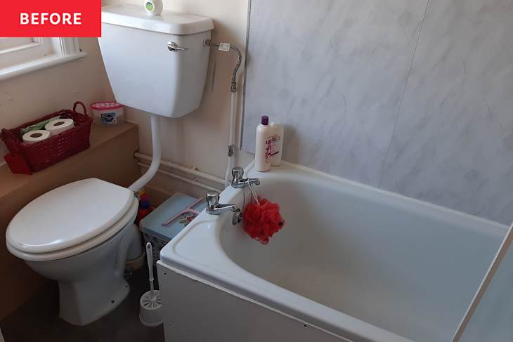 Small bathroom with a white toilet, bathtub, and toiletries on a shelf, featuring a red loofah and a basket of toilet paper.