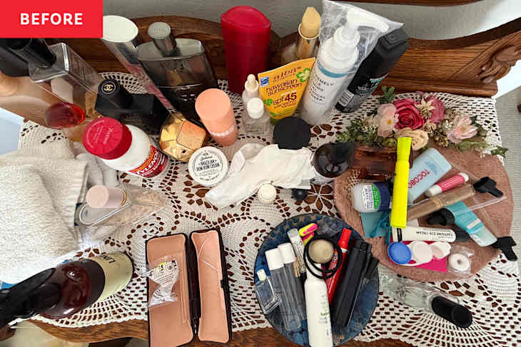 Cluttered vanity table with various skincare and beauty products, towels, and decorative flowers on a lace tablecloth.
