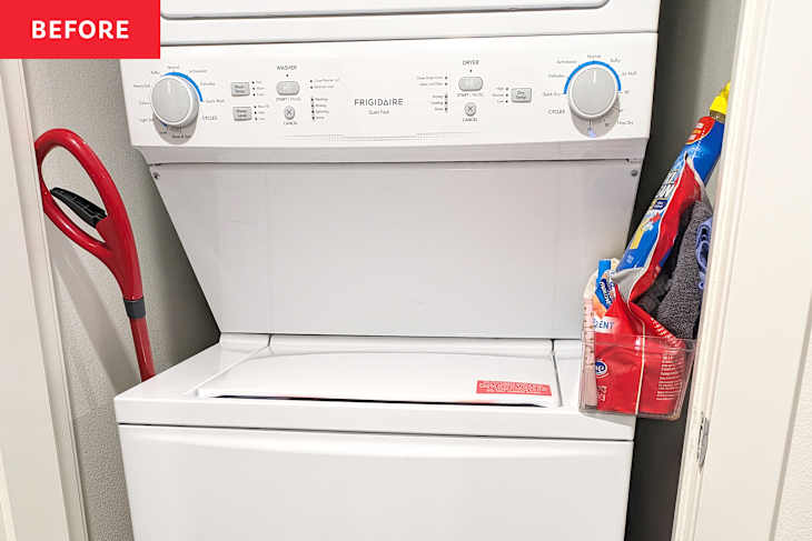 Washer and dryer stacked in a laundry nook with a red shovel leaning against the wall and laundry supplies in a clear container.