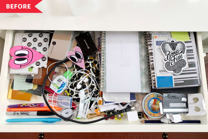 Messy drawer with notebooks, pens, cables, stickers, and various office supplies.