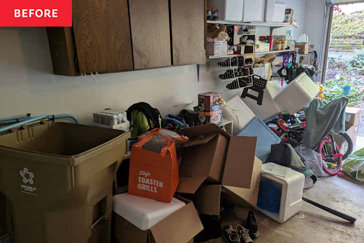 Cluttered garage space with cardboard boxes, a recycling bin, and various items including shoes, coolers, and a bicycle.