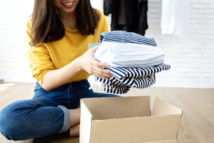 A woman sitting on the floor, putting clothes into a cardboard box for donation