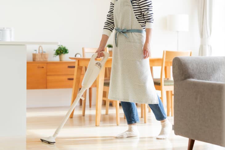 Person wearing an apron cleaning a kitchen and dining room with a stick vacuum cleaner