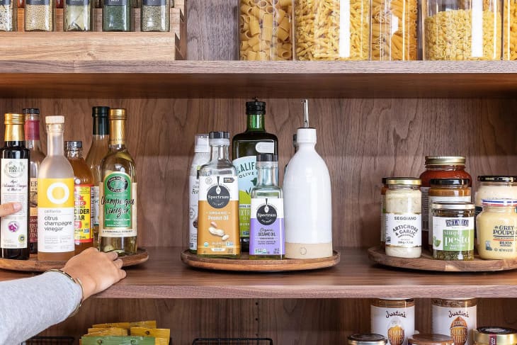 An organized wooden pantry shelf fitted with three wooden turntables holding an assortment of spices, condiments, and other pantry essentials.