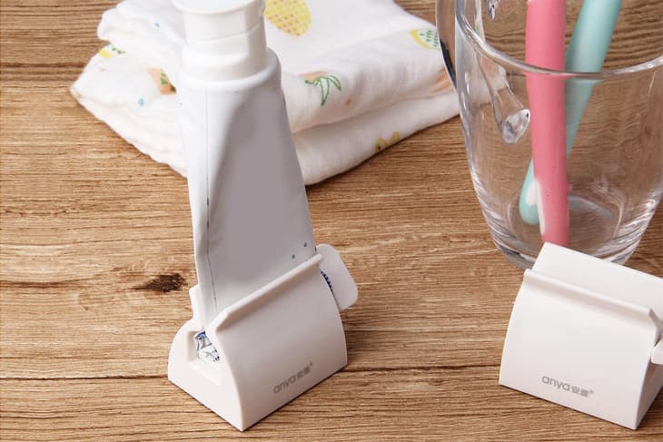 A toothpaste dispenser tool in use on a wooden bathroom countertop