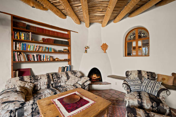 Cozy living room with patterned sofas, wooden coffee table, built-in bookshelves, and a lit corner fireplace.