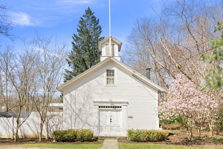 White clapboard building with a cupola, surrounded by trees and shrubs, under a clear blue sky.