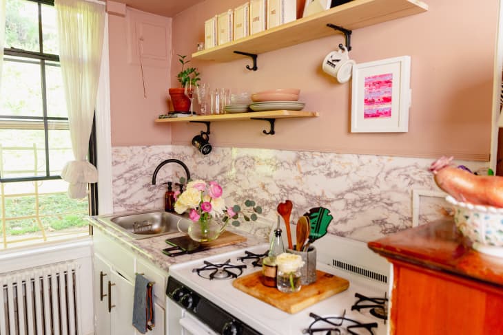 Pink kitchen with marble backsplash and open shelving.