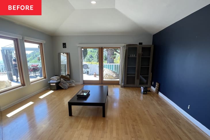 blue accent wall, wood floors, big picture windows, glass double doors, long rectangle room, low coffee table in center, arched ceiling, recess lighting, wardrobe in corner