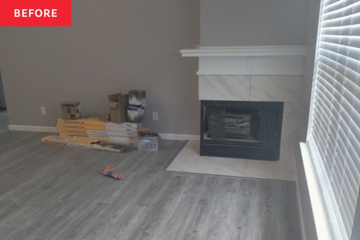 Fireplace in corner, wood planks in pile on floor, gray wood floor