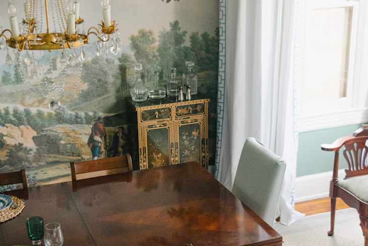 Dining room featuring a wooden table, vintage chandelier, decorative cabinet, and scenic wallpaper.