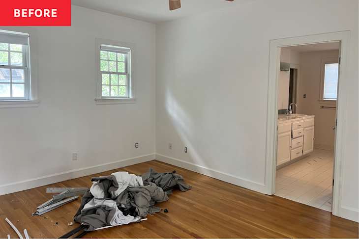 Cluttered room with hardwood floor, two windows, and an open doorway leading to a bathroom.