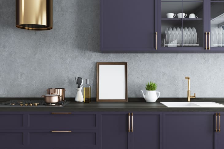 Concrete wall kitchen interior with a wooden floor and dark purple countertops.