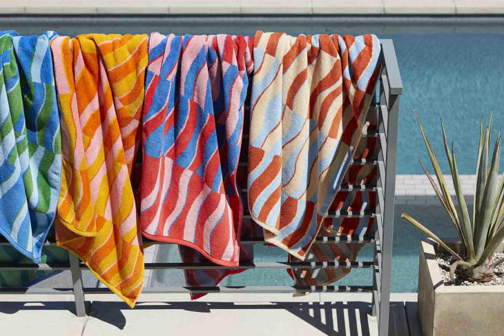 Large rack of Brooklinen colorful beach towels hanging by a pool outdoors