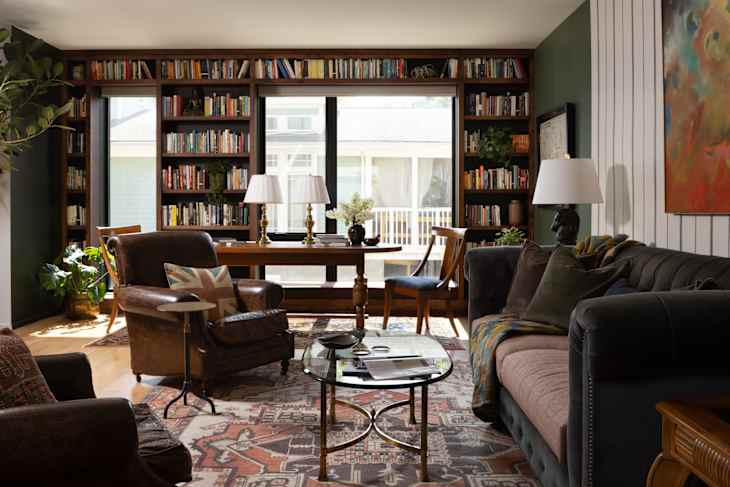 Library area of open concept space, showcases custom carpentry, antique table, vintage rug, thrifted lamps & chairs